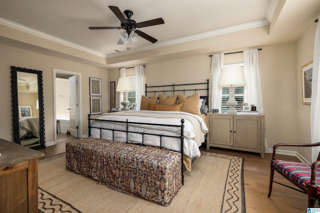 bedroom featuring ornamental molding, ceiling fan, light hardwood / wood-style floors, a raised ceiling, and ensuite bath