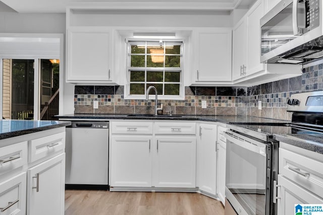 kitchen with dark stone counters, tasteful backsplash, white cabinets, appliances with stainless steel finishes, and light hardwood / wood-style flooring