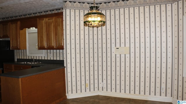 kitchen featuring baseboards, wallpapered walls, a sink, dark countertops, and brown cabinets