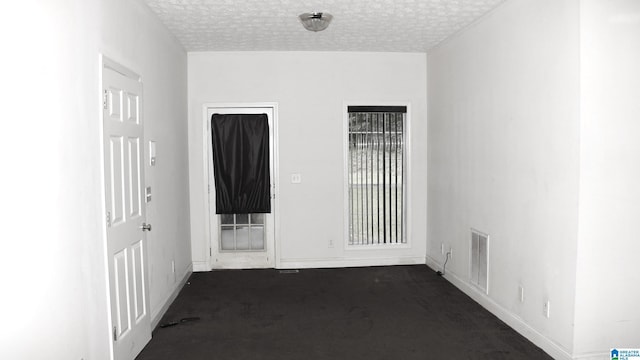 unfurnished room featuring baseboards, visible vents, dark colored carpet, and a textured ceiling