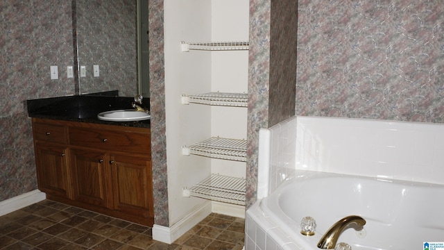 bathroom with baseboards, a bath, vanity, and wallpapered walls