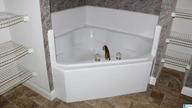 bathroom with stone finish floor, a jetted tub, and baseboards