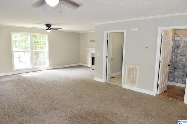 carpeted spare room with crown molding, ceiling fan, and a fireplace