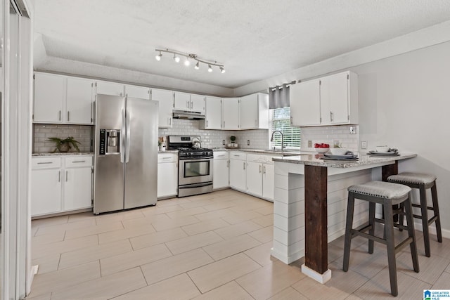 kitchen featuring white cabinetry, kitchen peninsula, a textured ceiling, a breakfast bar area, and appliances with stainless steel finishes