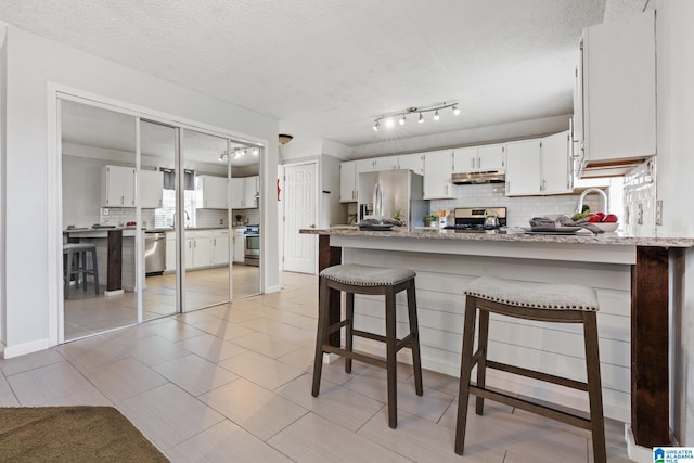 kitchen featuring white cabinets, a kitchen breakfast bar, a textured ceiling, and stainless steel appliances