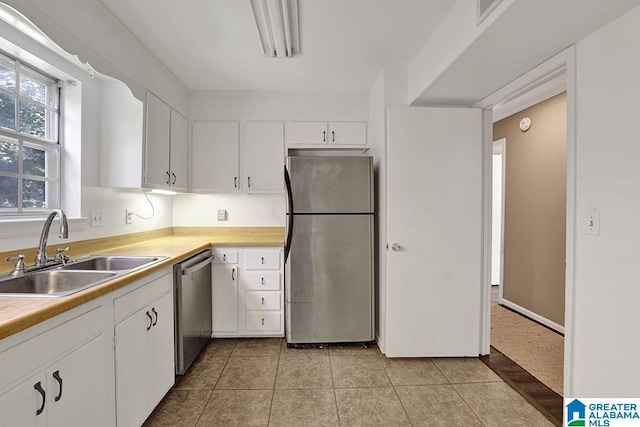 kitchen with light tile patterned flooring, sink, stainless steel appliances, and white cabinetry