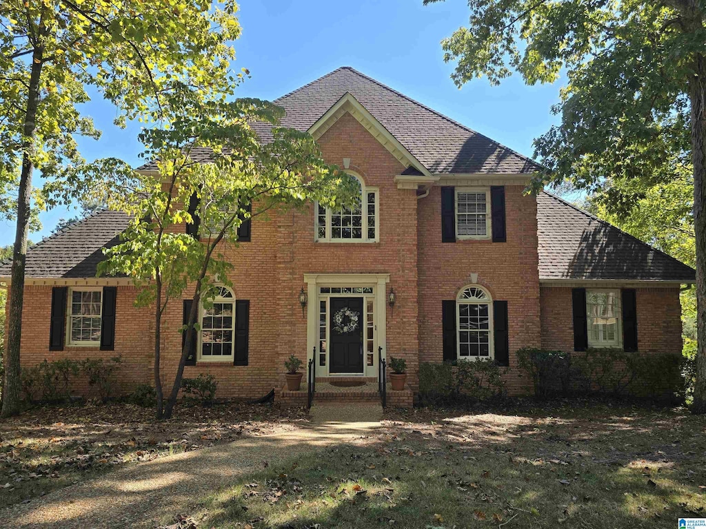 colonial-style house with brick siding, a shingled roof, and a front yard