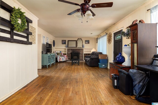 living room featuring hardwood / wood-style flooring, plenty of natural light, crown molding, and a brick fireplace