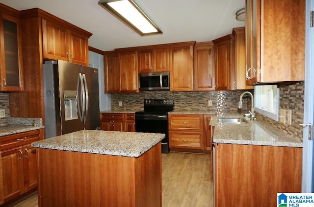 kitchen with light stone countertops, appliances with stainless steel finishes, a center island, sink, and light wood-type flooring