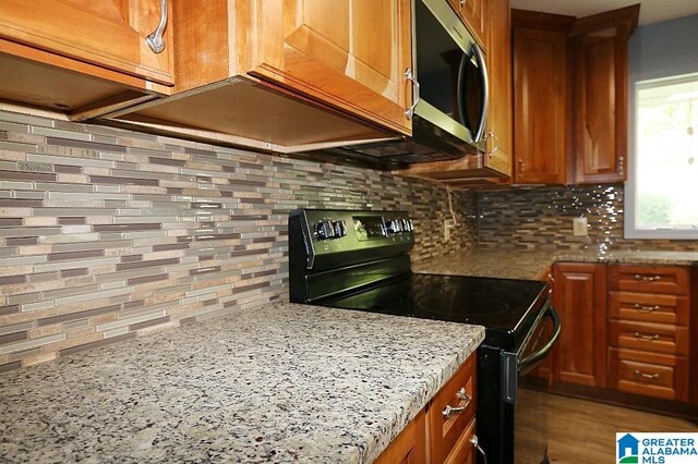 kitchen with black electric range, hardwood / wood-style floors, backsplash, and light stone countertops