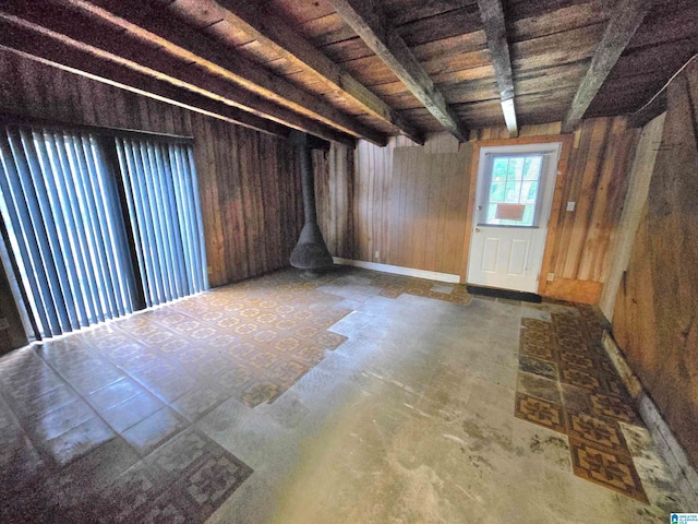 unfurnished room featuring wood walls, a wood stove, and beam ceiling