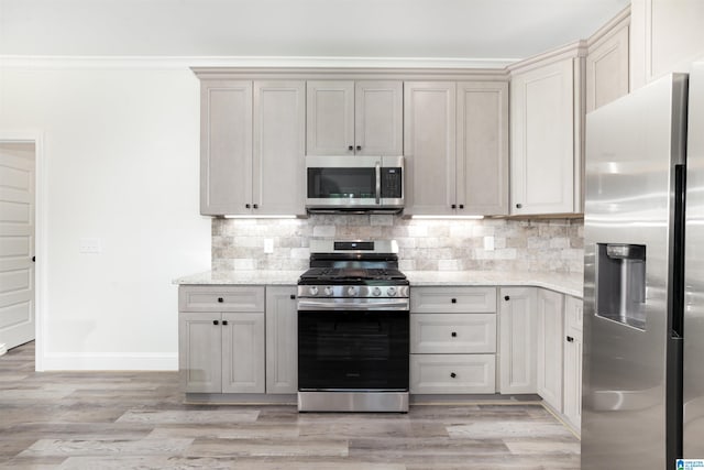 kitchen with stainless steel appliances, gray cabinetry, light stone counters, light hardwood / wood-style floors, and decorative backsplash