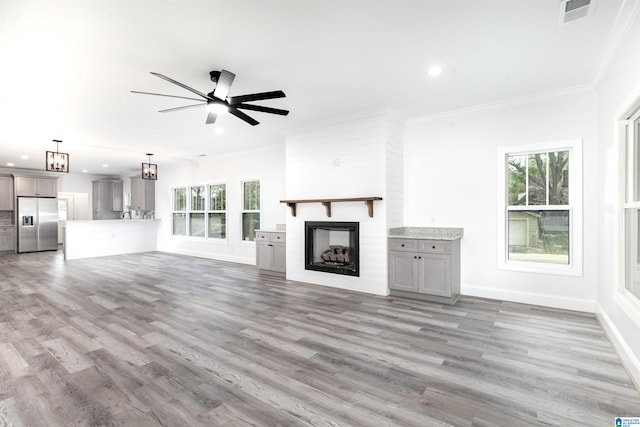 unfurnished living room featuring ceiling fan, ornamental molding, hardwood / wood-style floors, and a large fireplace