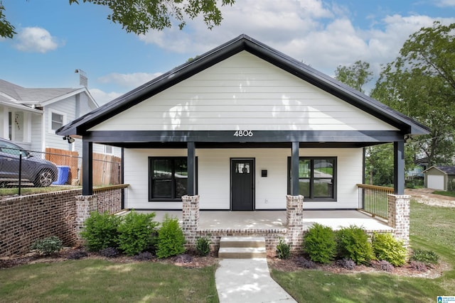 view of front of home featuring a garage, a front lawn, an outbuilding, and covered porch