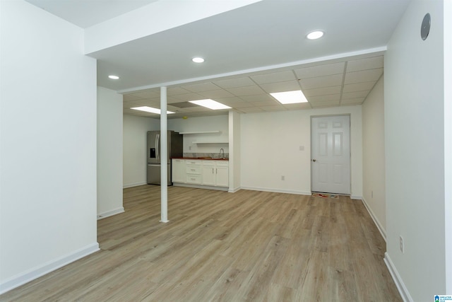 unfurnished living room featuring light hardwood / wood-style floors, a drop ceiling, and sink