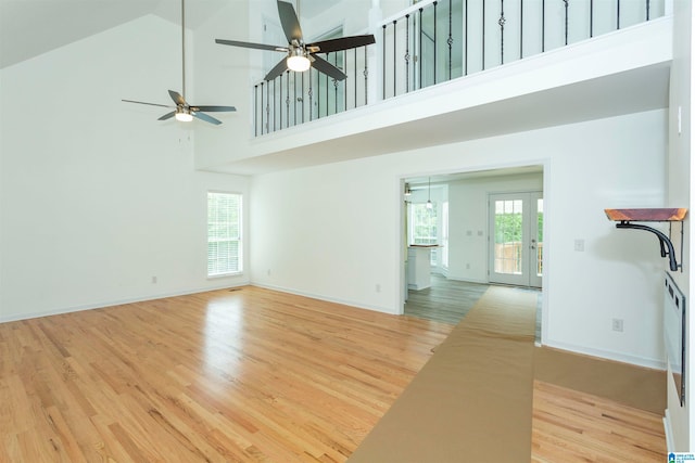 unfurnished living room with ceiling fan, light wood-type flooring, and high vaulted ceiling