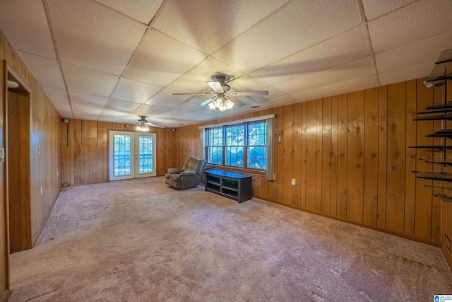 unfurnished living room featuring carpet flooring, wood walls, ceiling fan, and a drop ceiling