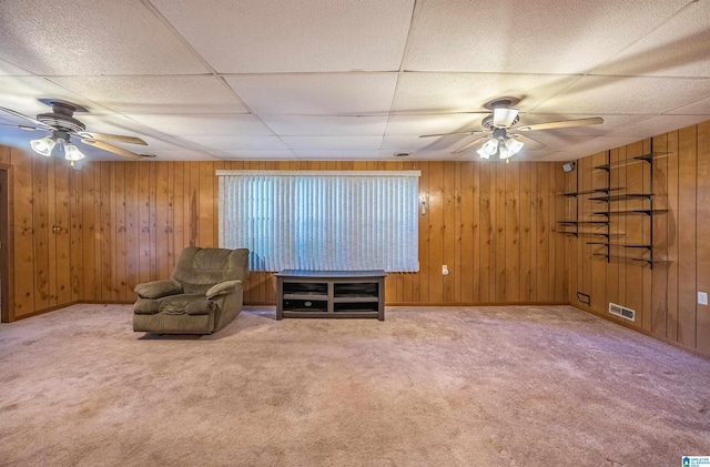 unfurnished room featuring a drop ceiling, wood walls, ceiling fan, and carpet flooring