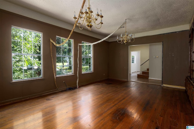 spare room featuring a textured ceiling, an inviting chandelier, wood-type flooring, and plenty of natural light