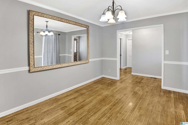 spare room with wood-type flooring, crown molding, and an inviting chandelier