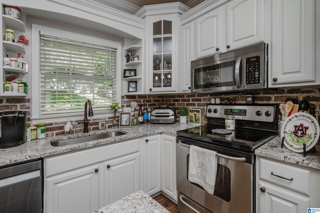 kitchen with appliances with stainless steel finishes, white cabinets, sink, light stone counters, and hardwood / wood-style flooring