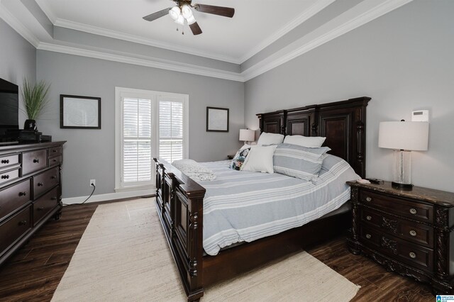 bedroom featuring dark wood-type flooring, a raised ceiling, ornamental molding, and ceiling fan