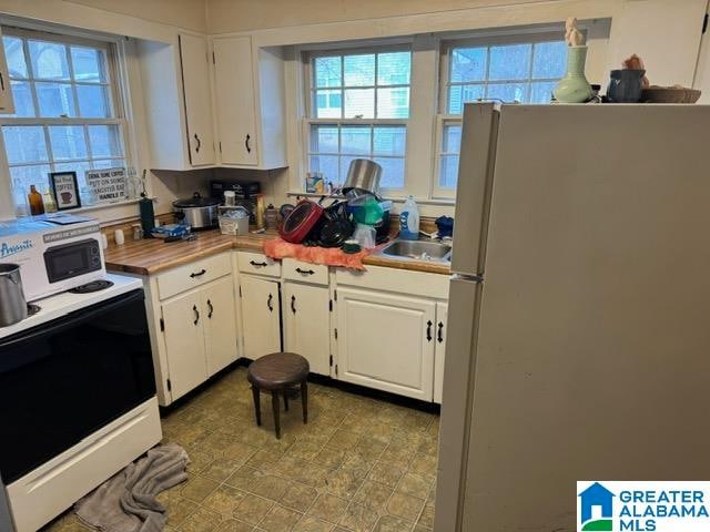 kitchen with white cabinets, light tile patterned flooring, white appliances, and sink