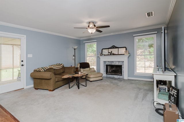 carpeted living room with crown molding, ceiling fan, a healthy amount of sunlight, and a premium fireplace