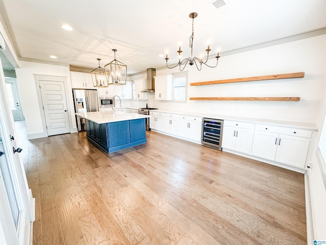 kitchen featuring wall chimney range hood, hanging light fixtures, stainless steel appliances, an island with sink, and beverage cooler