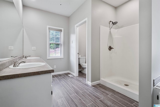 bathroom with dual vanity, toilet, hardwood / wood-style flooring, and walk in shower