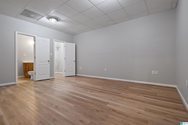 unfurnished bedroom featuring connected bathroom, a drop ceiling, and light hardwood / wood-style flooring