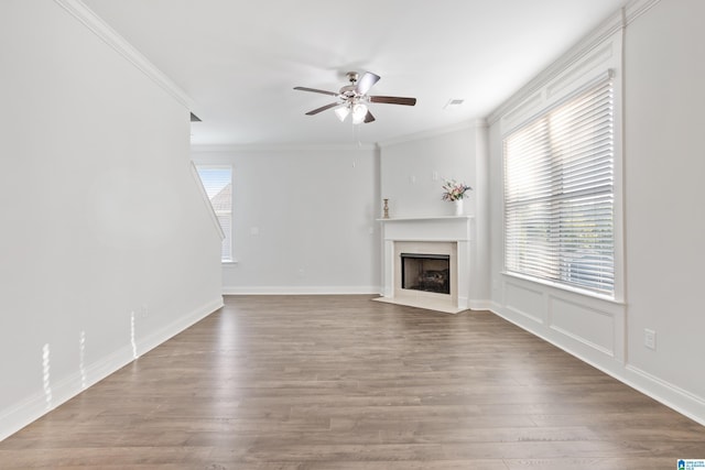 unfurnished living room with ceiling fan, wood finished floors, a fireplace with flush hearth, visible vents, and crown molding