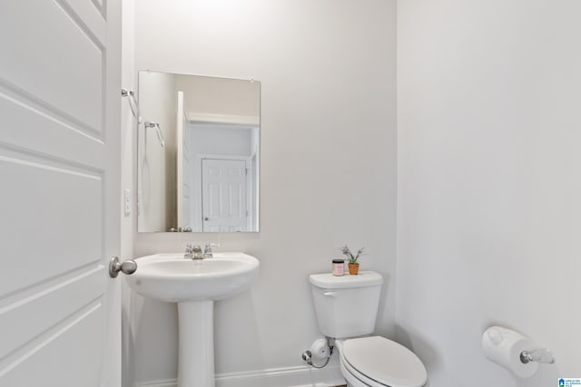 half bathroom with toilet, baseboards, and a sink