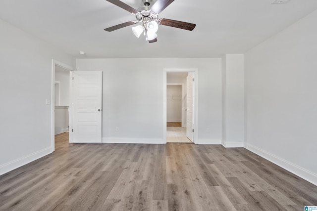 unfurnished bedroom featuring a spacious closet, ceiling fan, light wood-type flooring, and a closet