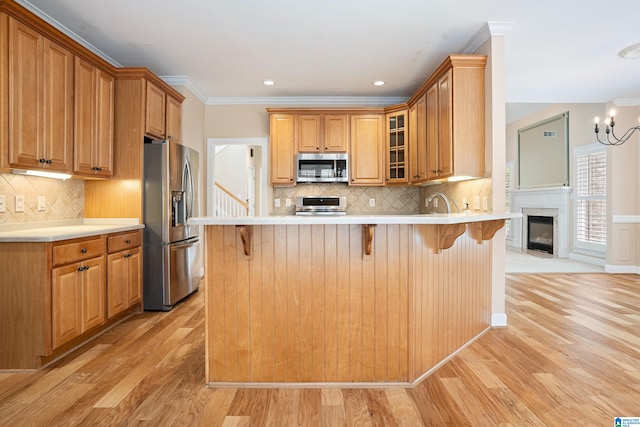 kitchen with stainless steel appliances, kitchen peninsula, backsplash, light wood-type flooring, and a chandelier