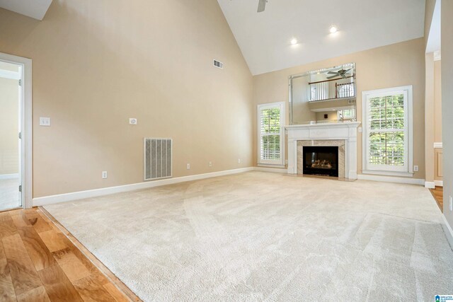 unfurnished living room featuring a premium fireplace, ceiling fan, light hardwood / wood-style floors, and high vaulted ceiling