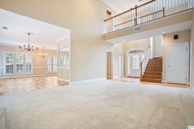 unfurnished living room with light carpet, a notable chandelier, crown molding, and a high ceiling