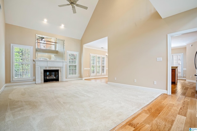 unfurnished living room with a premium fireplace, light colored carpet, high vaulted ceiling, ceiling fan, and ornamental molding