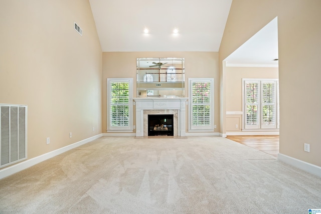 unfurnished living room featuring a high end fireplace, high vaulted ceiling, crown molding, and light hardwood / wood-style floors