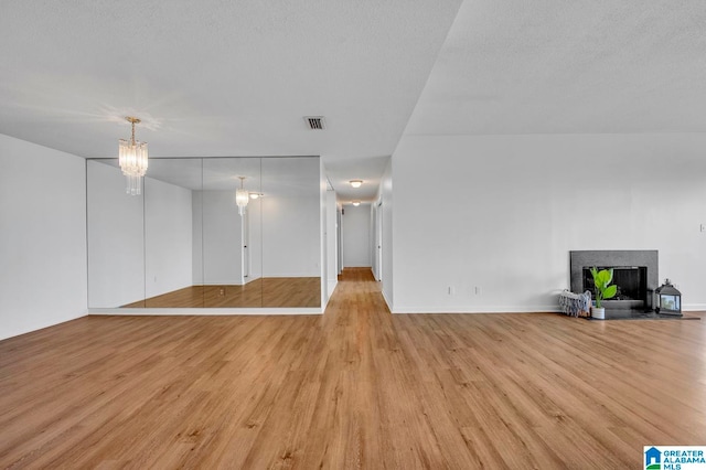 unfurnished living room with light wood-type flooring, a notable chandelier, and a textured ceiling