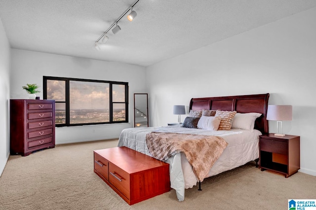 bedroom featuring track lighting, light colored carpet, and a textured ceiling