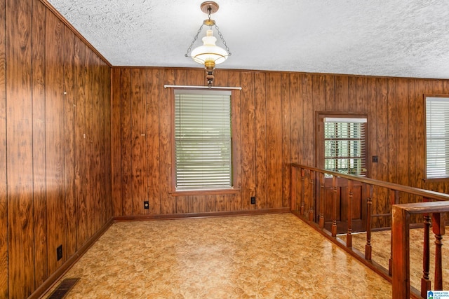 unfurnished room with a textured ceiling and wood walls