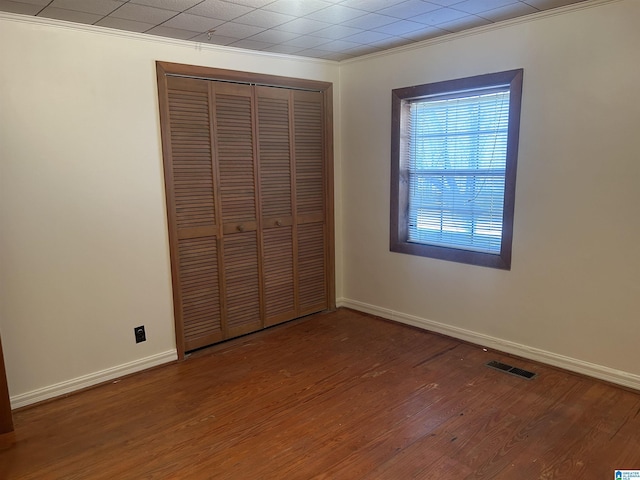 unfurnished bedroom with hardwood / wood-style floors, crown molding, and a closet