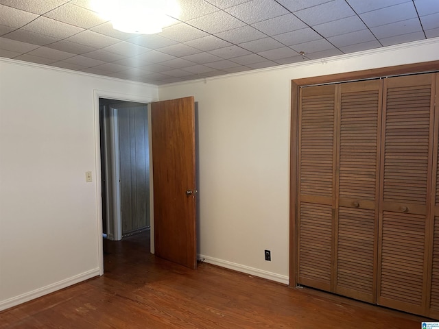 unfurnished bedroom with wood-type flooring, crown molding, and a closet