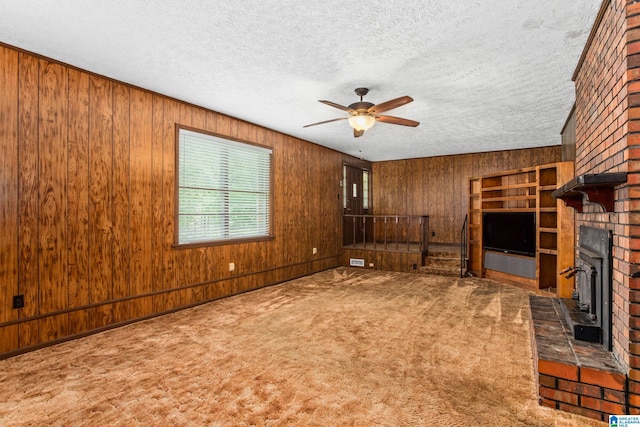 unfurnished living room featuring ceiling fan, wood walls, a brick fireplace, and a textured ceiling