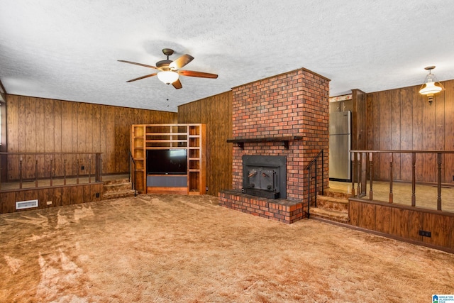 unfurnished living room featuring ceiling fan, wooden walls, a textured ceiling, and carpet