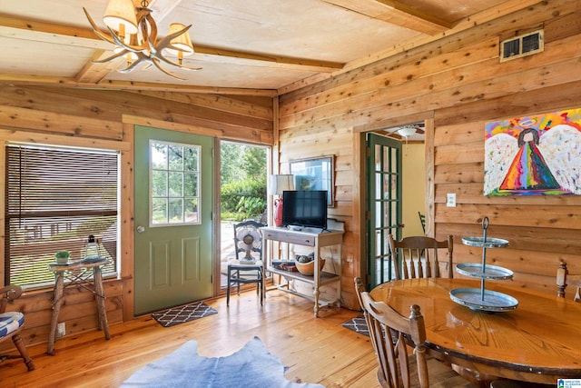 dining room with wood walls, light hardwood / wood-style floors, an inviting chandelier, and lofted ceiling with beams