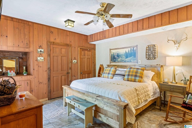 bedroom with wood walls, light tile patterned floors, ceiling fan, and a textured ceiling