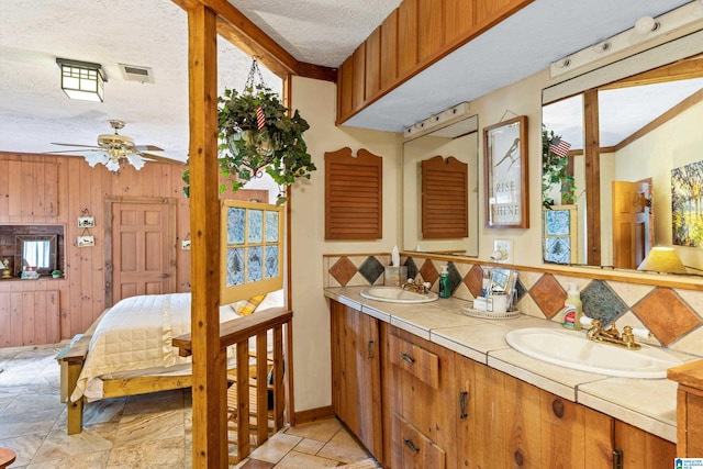 bathroom with decorative backsplash, tile patterned floors, a textured ceiling, dual bowl vanity, and ceiling fan