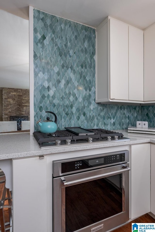 kitchen with a breakfast bar, backsplash, oven, white cabinetry, and hardwood / wood-style flooring